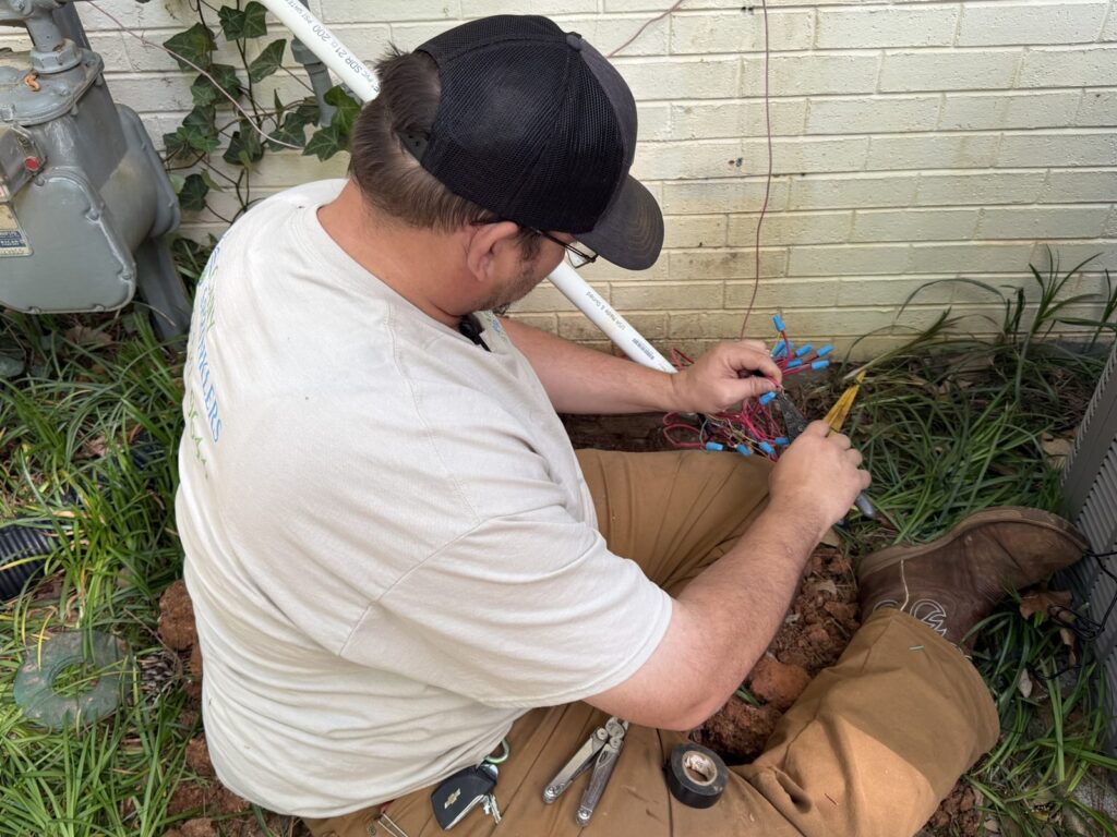 Technician splicing and repairing irrigation valve wiring beside a home in Cary, NC