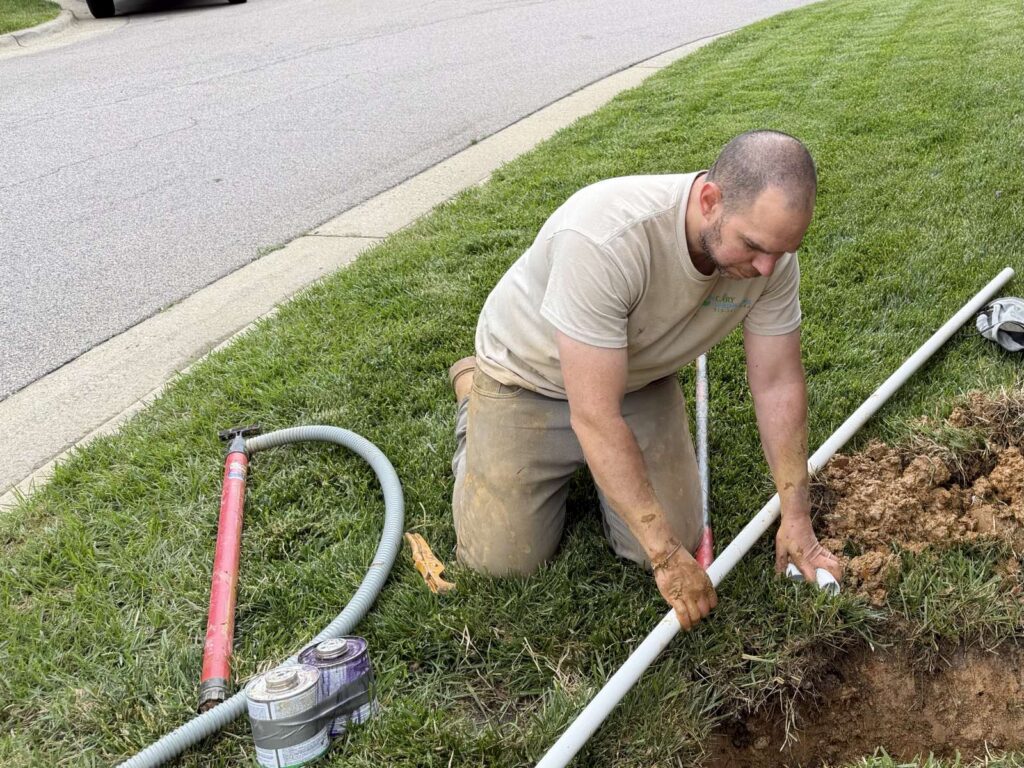 Cary Sprinklers technician adjusting a pop-up sprinkler head along a curb lawn in Cary, NC