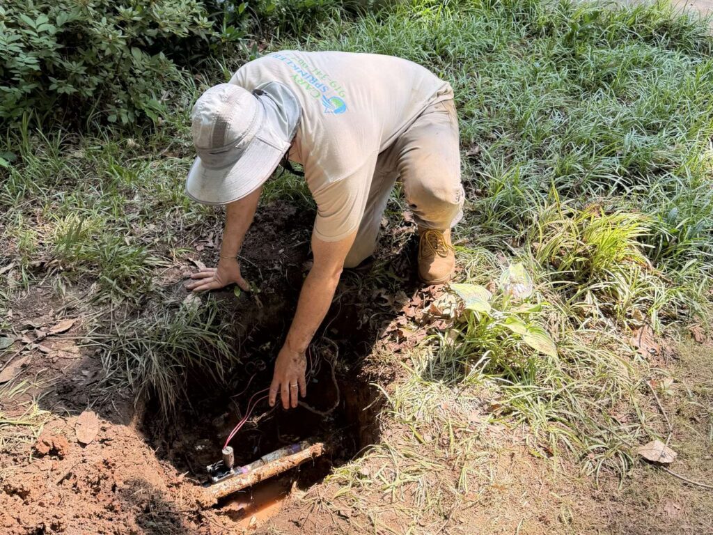 Cary Sprinklers technician locating and repairing a sprinkler leak in a landscape bed in Cary, NC