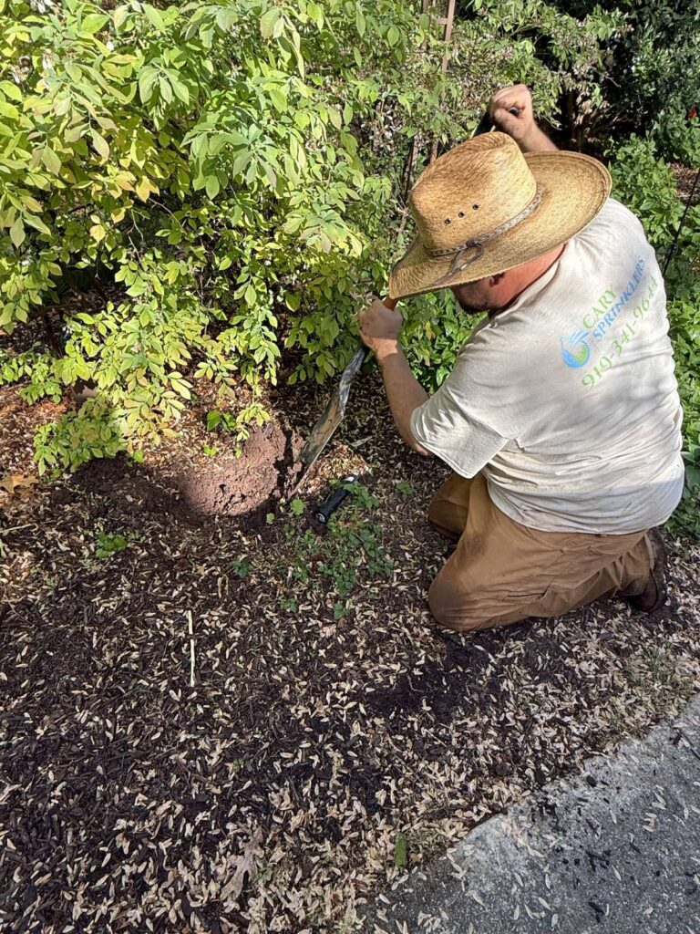 Technician servicing a sprinkler head within a shrub bed in the Cary, NC area